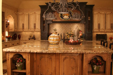 Foto de cocina comedor lineal mediterránea de tamaño medio con fregadero bajoencimera, armarios con paneles con relieve, puertas de armario de madera en tonos medios, encimera de mármol, salpicadero beige, salpicadero de azulejos de piedra, electrodomésticos negros, suelo de travertino y una isla