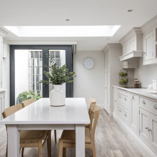 This is an example of a medium sized classic galley kitchen/diner in London with a submerged sink, shaker cabinets, grey cabinets, white splashback, integrated appliances, no island, grey floors and white worktops.