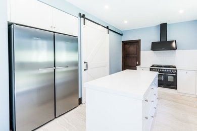 Example of a large classic porcelain tile kitchen pantry design in Melbourne with a farmhouse sink, recessed-panel cabinets, white cabinets, quartz countertops, white backsplash, ceramic backsplash, black appliances and an island
