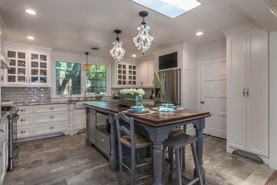 Mid-sized cottage u-shaped ceramic tile and gray floor eat-in kitchen photo in Dallas with a farmhouse sink, shaker cabinets, white cabinets, wood countertops, gray backsplash, subway tile backsplash, stainless steel appliances and an island