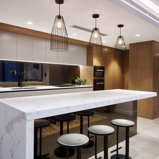 Inspiration for a large contemporary l-shaped kitchen in Perth with an undermount sink, flat-panel cabinets, white cabinets, black splashback, glass sheet splashback, panelled appliances, with island, grey floor and white benchtop.