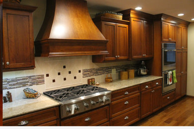 Cette photo montre une grande cuisine parallèle chic en bois brun fermée avec un placard à porte shaker, un plan de travail en quartz, une crédence beige, un électroménager en acier inoxydable, un sol en bois brun, un sol marron, un évier encastré et une péninsule.