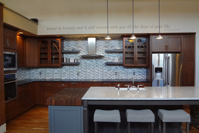 Elegant eat-in kitchen photo in Boston with a farmhouse sink, glass-front cabinets, soapstone countertops, blue backsplash, glass tile backsplash, stainless steel appliances and an island