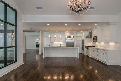 Example of a large transitional l-shaped medium tone wood floor and brown floor eat-in kitchen design in Dallas with an undermount sink, shaker cabinets, white cabinets, marble countertops, white backsplash, glass tile backsplash, stainless steel appliances and an island