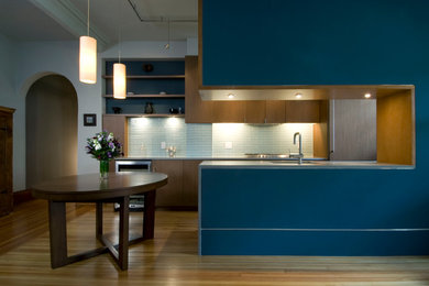 Стильный дизайн: параллельная кухня в современном стиле с обеденным столом, плоскими фасадами, фасадами цвета дерева среднего тона, фартуком из стеклянной плитки, цветной техникой, полуостровом, одинарной мойкой и синим фартуком - последний тренд