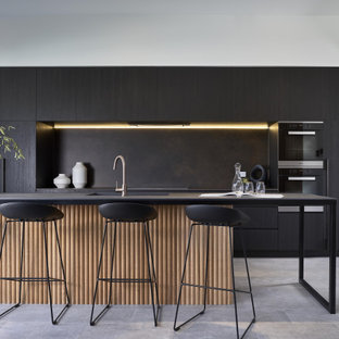 Modern galley kitchen in Brisbane with an undermount sink, flat-panel cabinets, black cabinets, black splashback, stainless steel appliances, with island and grey floor.