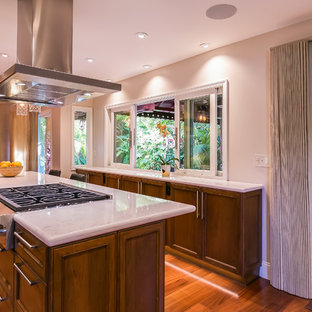 Idées déco pour une grand cuisine américaine parallèle contemporaine avec un évier encastré, un placard avec porte à panneau encastré, des portes de placard en bois sombre, un plan de travail en quartz modifié, une crédence blanche, une crédence en dalle de pierre, un électroménager en acier inoxydable, un îlot central, un sol marron, un sol en bois brun et un plan de travail blanc.