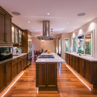 This is an example of a large contemporary galley eat-in kitchen in San Francisco with an undermount sink, recessed-panel cabinets, dark wood cabinets, quartz benchtops, white splashback, stone slab splashback, stainless steel appliances, with island, brown floor, medium hardwood floors and white benchtop.