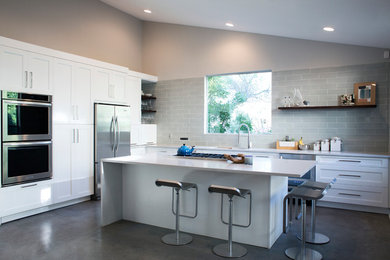 Inspiration for a mid-sized modern l-shaped concrete floor eat-in kitchen remodel in Dallas with white cabinets, quartzite countertops, an undermount sink, shaker cabinets, green backsplash, glass tile backsplash, stainless steel appliances and an island