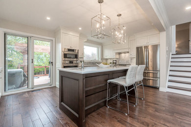 Photo of a large traditional u-shaped open plan kitchen in Toronto with a submerged sink, raised-panel cabinets, white cabinets, quartz worktops, grey splashback, marble splashback, stainless steel appliances, medium hardwood flooring, an island and brown floors.