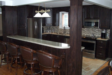 Photo of a large u-shaped open plan kitchen in Toronto with a submerged sink, dark wood cabinets, stainless steel appliances, a breakfast bar, granite worktops, mosaic tiled splashback and travertine flooring.