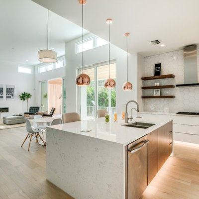 Example of a mid-sized trendy l-shaped light wood floor and beige floor eat-in kitchen design in Tampa with a double-bowl sink, flat-panel cabinets, white cabinets, quartz countertops, white backsplash, ceramic backsplash, stainless steel appliances, an island and white countertops