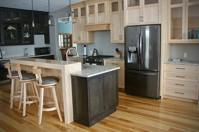 Cette photo montre une cuisine américaine en bois clair avec un évier 2 bacs, un placard avec porte à panneau encastré, un plan de travail en granite, un électroménager en acier inoxydable, parquet clair, îlot et un plan de travail gris.