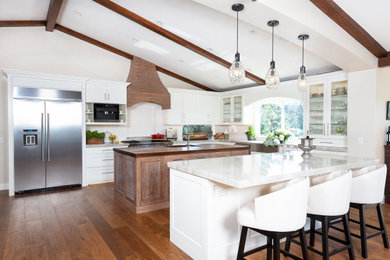 Huge trendy u-shaped medium tone wood floor and brown floor open concept kitchen photo in San Diego with a farmhouse sink, shaker cabinets, white cabinets, granite countertops, white backsplash, subway tile backsplash, stainless steel appliances, two islands and beige countertops
