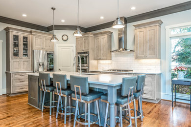Example of a large transitional l-shaped medium tone wood floor and brown floor eat-in kitchen design in Atlanta with a farmhouse sink, raised-panel cabinets, beige cabinets, white backsplash, subway tile backsplash, stainless steel appliances, an island and white countertops
