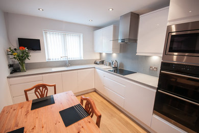 Large contemporary kitchen/diner in Sussex with a built-in sink, flat-panel cabinets, composite countertops, grey splashback, stainless steel appliances, no island and grey worktops.