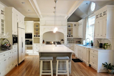 Exempel på ett stort klassiskt kök, med en undermonterad diskho, luckor med profilerade fronter, vita skåp, bänkskiva i kvartsit, vitt stänkskydd, stänkskydd i keramik, rostfria vitvaror, mellanmörkt trägolv, en köksö och brunt golv