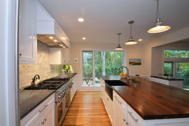 Example of a large trendy galley plywood floor eat-in kitchen design in Philadelphia with an undermount sink, shaker cabinets, white cabinets, wood countertops, white backsplash, stone tile backsplash, an island and stainless steel appliances