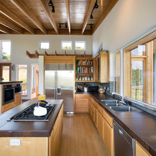 Cette image montre une grand cuisine ouverte parallèle design avec un électroménager en acier inoxydable, un évier 3 bacs, des portes de placard en bois brun, une crédence en carreau de céramique, un sol en bois brun, un îlot central, un placard avec porte à panneau encastré, une crédence multicolore et un sol marron.