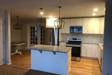Mid-sized transitional l-shaped light wood floor and brown floor open concept kitchen photo in Charlotte with recessed-panel cabinets, white cabinets, granite countertops, an island, stainless steel appliances, an undermount sink and gray countertops