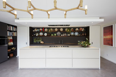 Large eclectic open plan kitchen in London with a single-bowl sink, flat-panel cabinets, beige cabinets, quartz worktops, integrated appliances, concrete flooring, an island, grey floors and beige worktops.