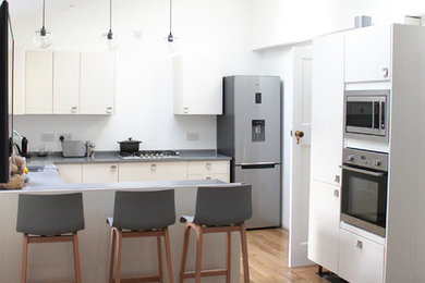 Moderne Küche mit flächenbündigen Schrankfronten, weißen Schränken, Mineralwerkstoff-Arbeitsplatte, Küchengeräten aus Edelstahl, hellem Holzboden und grauer Arbeitsplatte in Glasgow