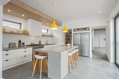 Inspiration for a medium sized industrial single-wall kitchen in Dublin with flat-panel cabinets, white cabinets, concrete worktops, white splashback, concrete flooring, an island, grey floors and stainless steel appliances.