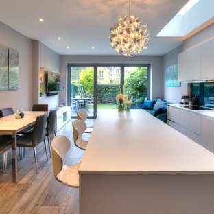 Photo of a medium sized contemporary single-wall open plan kitchen in London with flat-panel cabinets, white cabinets, an island, white worktops, a submerged sink and glass sheet splashback.