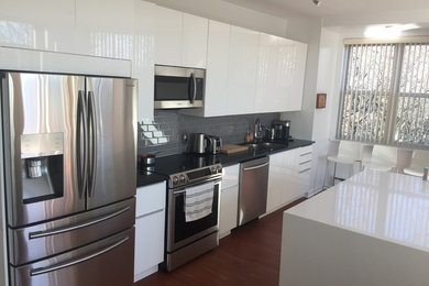 This is an example of a medium sized contemporary single-wall kitchen/diner in Other with a double-bowl sink, flat-panel cabinets, white cabinets, engineered stone countertops, grey splashback, metro tiled splashback, stainless steel appliances, dark hardwood flooring, an island and brown floors.