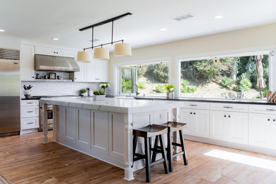 Inspiration for a large cottage medium tone wood floor and brown floor open concept kitchen remodel in Orange County with a farmhouse sink, shaker cabinets, white cabinets, solid surface countertops, black backsplash, porcelain backsplash, stainless steel appliances and an island