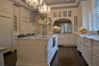 Enclosed kitchen - large traditional u-shaped dark wood floor enclosed kitchen idea in New York with a farmhouse sink, raised-panel cabinets, white cabinets, marble countertops, gray backsplash, stone tile backsplash, stainless steel appliances and an island
