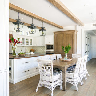Design ideas for a large tropical u-shaped eat-in kitchen in Orange County with a double-bowl sink, shaker cabinets, white cabinets, wood benchtops, white splashback, subway tile splashback, stainless steel appliances, medium hardwood floors, with island, brown floor and brown benchtop.