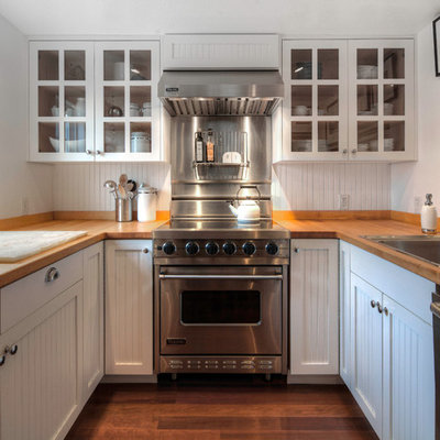 Enclosed kitchen - coastal u-shaped medium tone wood floor enclosed kitchen idea in Seattle with a drop-in sink, white cabinets, stainless steel appliances, white backsplash and wood countertops