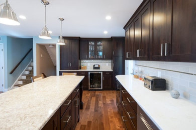 Example of a large transitional medium tone wood floor and brown floor kitchen design in Philadelphia with shaker cabinets, dark wood cabinets, gray backsplash, subway tile backsplash, stainless steel appliances and an island