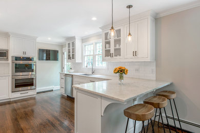 Inspiration for a mid-sized transitional l-shaped dark wood floor open concept kitchen remodel in New York with an undermount sink, beaded inset cabinets, white cabinets, marble countertops, white backsplash, ceramic backsplash, stainless steel appliances and a peninsula
