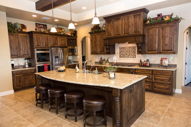 Elegant kitchen photo in Austin with raised-panel cabinets, dark wood cabinets, granite countertops, beige backsplash, stone tile backsplash, stainless steel appliances and an island