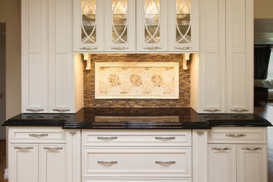 Example of a large classic u-shaped medium tone wood floor enclosed kitchen design in St Louis with recessed-panel cabinets, white cabinets, granite countertops, multicolored backsplash, mosaic tile backsplash and an island
