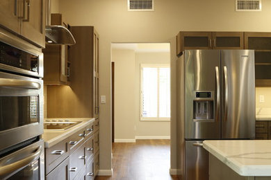 Example of a small trendy l-shaped vinyl floor and brown floor enclosed kitchen design in Phoenix with a single-bowl sink, shaker cabinets, brown cabinets, quartz countertops, gray backsplash, glass tile backsplash, stainless steel appliances, a peninsula and white countertops