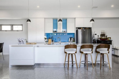パースにある中くらいなモダンスタイルのおしゃれなキッチン (白いキャビネット、青いキッチンパネル、ガラス板のキッチンパネル、コンクリートの床、グレーの床、フラットパネル扉のキャビネット、御影石カウンター) の写真