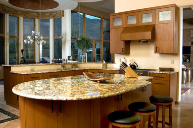 Large contemporary l-shaped kitchen pantry in Phoenix with flat-panel cabinets, medium wood cabinets, granite worktops, stainless steel appliances, travertine flooring, an island and a submerged sink.