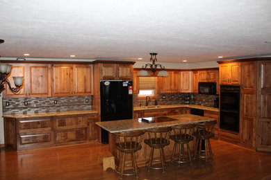Example of a large mountain style l-shaped medium tone wood floor and brown floor open concept kitchen design in Other with an undermount sink, raised-panel cabinets, brown cabinets, quartzite countertops, metallic backsplash, black appliances, an island and brown countertops