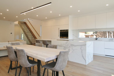 Inspiration for a mid-sized modern single-wall light wood floor and brown floor eat-in kitchen remodel in Ottawa with an undermount sink, flat-panel cabinets, white cabinets, marble countertops, gray backsplash, marble backsplash, paneled appliances, an island and gray countertops