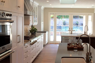 Inspiration for a craftsman light wood floor kitchen remodel in San Diego with a farmhouse sink, granite countertops, beige backsplash, stainless steel appliances and two islands