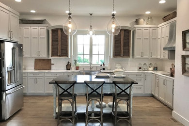 Inspiration for a large timeless u-shaped light wood floor and brown floor eat-in kitchen remodel in Other with a farmhouse sink, flat-panel cabinets, gray cabinets, marble countertops, white backsplash, ceramic backsplash, stainless steel appliances and an island