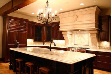 Eat-in kitchen - mid-sized traditional l-shaped medium tone wood floor and brown floor eat-in kitchen idea in Denver with an undermount sink, raised-panel cabinets, dark wood cabinets, granite countertops, beige backsplash, travertine backsplash, paneled appliances and an island