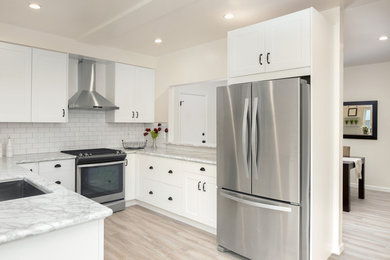 Mid-sized transitional u-shaped light wood floor and beige floor open concept kitchen photo in Boston with an undermount sink, shaker cabinets, white cabinets, marble countertops, white backsplash, subway tile backsplash, stainless steel appliances, a peninsula and gray countertops
