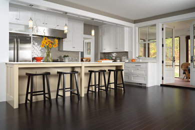 Example of a large transitional l-shaped dark wood floor and brown floor kitchen design in Other with an undermount sink, shaker cabinets, white cabinets, solid surface countertops, gray backsplash, subway tile backsplash, stainless steel appliances and an island