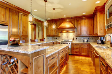 Inspiration for a mid-sized timeless u-shaped medium tone wood floor and brown floor enclosed kitchen remodel in Houston with an undermount sink, recessed-panel cabinets, medium tone wood cabinets, granite countertops, brown backsplash, stone tile backsplash, stainless steel appliances and an island