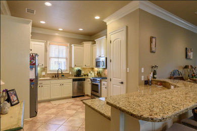 Example of a mid-sized classic u-shaped beige floor open concept kitchen design in New Orleans with a double-bowl sink, raised-panel cabinets, white cabinets, granite countertops, beige backsplash, stone tile backsplash, stainless steel appliances and a peninsula