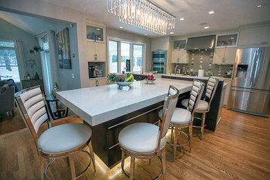 Large trendy u-shaped medium tone wood floor eat-in kitchen photo in Boston with an undermount sink, flat-panel cabinets, white cabinets, quartz countertops, stainless steel appliances, an island and mirror backsplash